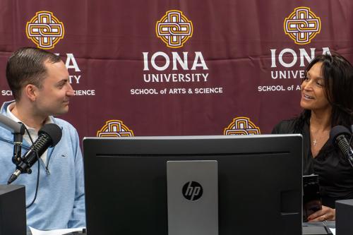 Matthew Ricker and Victoria Bruno sit at microphones facing each other and smiling during a conversation in the Iona University podcast studio.