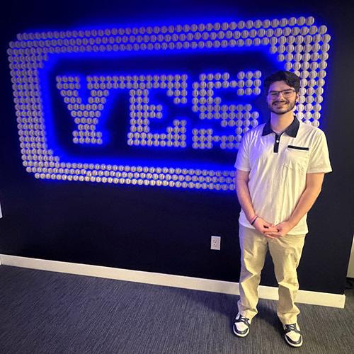 Landon in front of the YES logo at his internship.