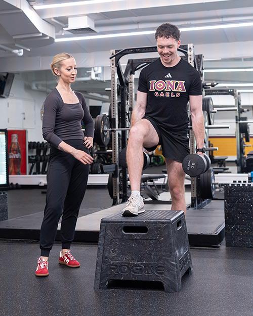 A professor works with a Health and Wellness major doing dumbbell box steps.