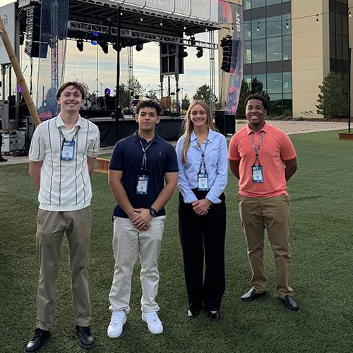 Four Iona University students wear event lanyards while posing together on an outdoor lawn at the BNY Insite conference.