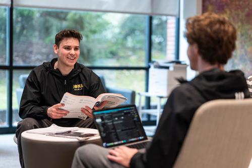 Two undeclared students talk in a study space with large windows. 