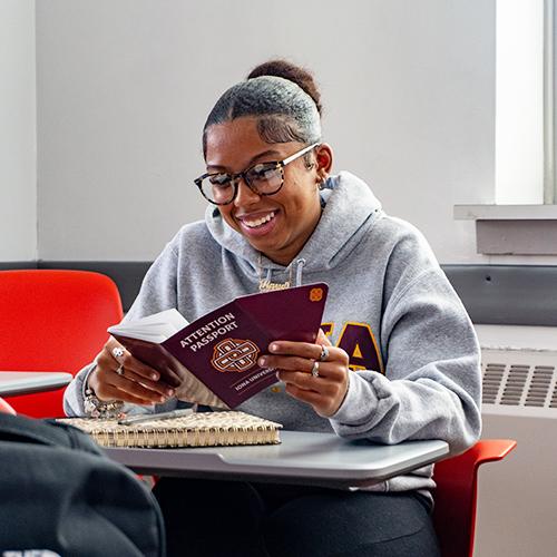 A student smiles at her desk opening up the Attention Passport.