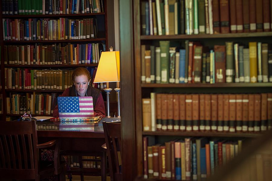 A student works alone in the library. Her laptop has an American flag overlay.