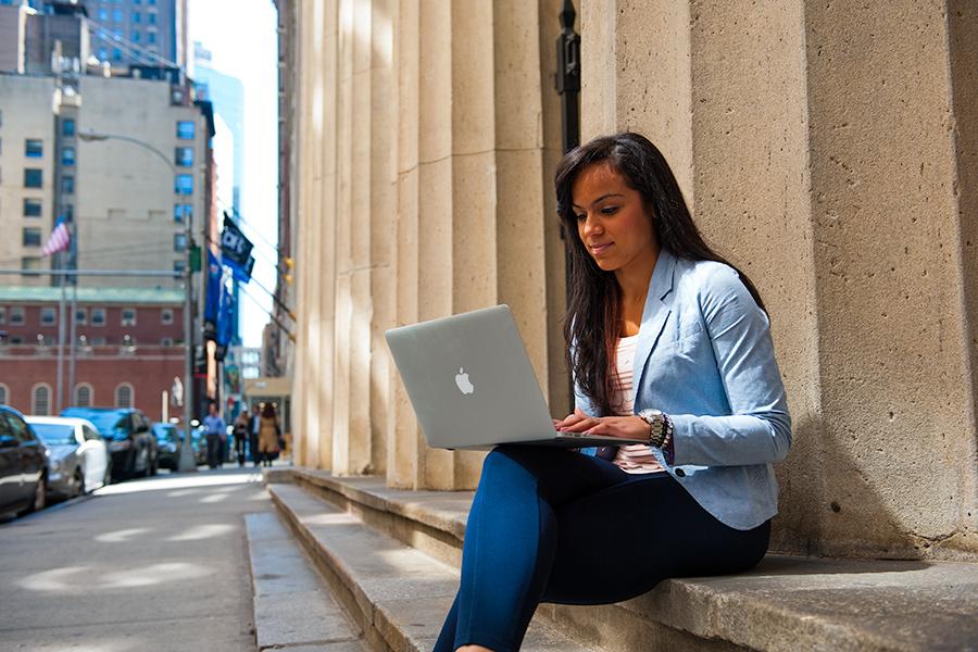 A student sits in New York City and works on her laptop.