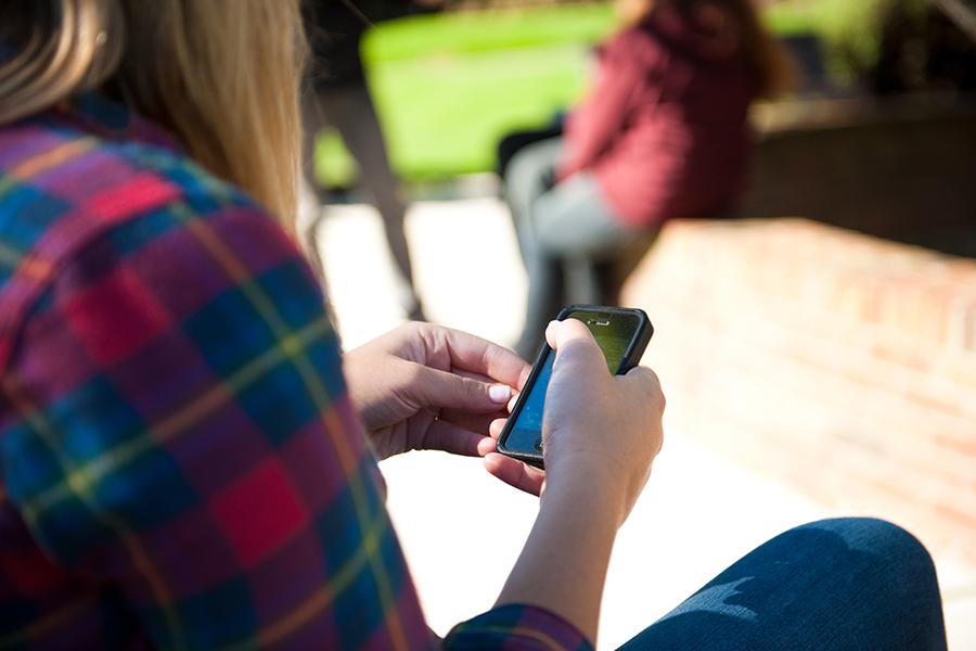 A person in a flannel shirt sits on a bench and uses an iPhone.