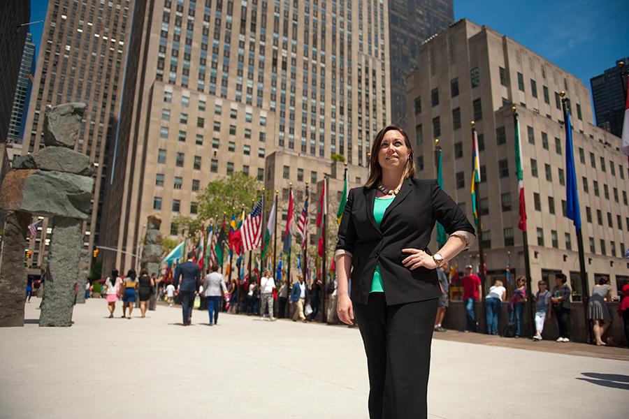 A student visits Rockafeller center in New York City and stands near the flags of the world.